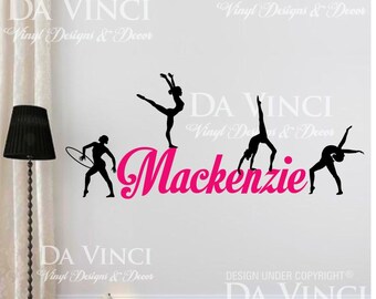 May include: A pink vinyl wall decal with the name "Mackenzie" in a cursive font. Three black silhouettes of gymnasts are positioned above the name. The decal includes the text "DA VINCI Vinyl Designs & Decor" at the top and bottom of the image.