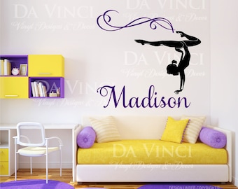 May include: A purple and black wall decal featuring a silhouette of a gymnast doing a handstand with a ribbon. The decal includes the name "Madison" in a purple script font.