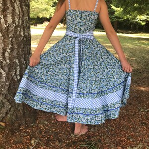Puede incluir: Un vestido de estampado floral azul y blanco con ribete de vichy y una cinta a juego. El vestido tiene un corpi&ntilde;o ajustado y una falda completa.
