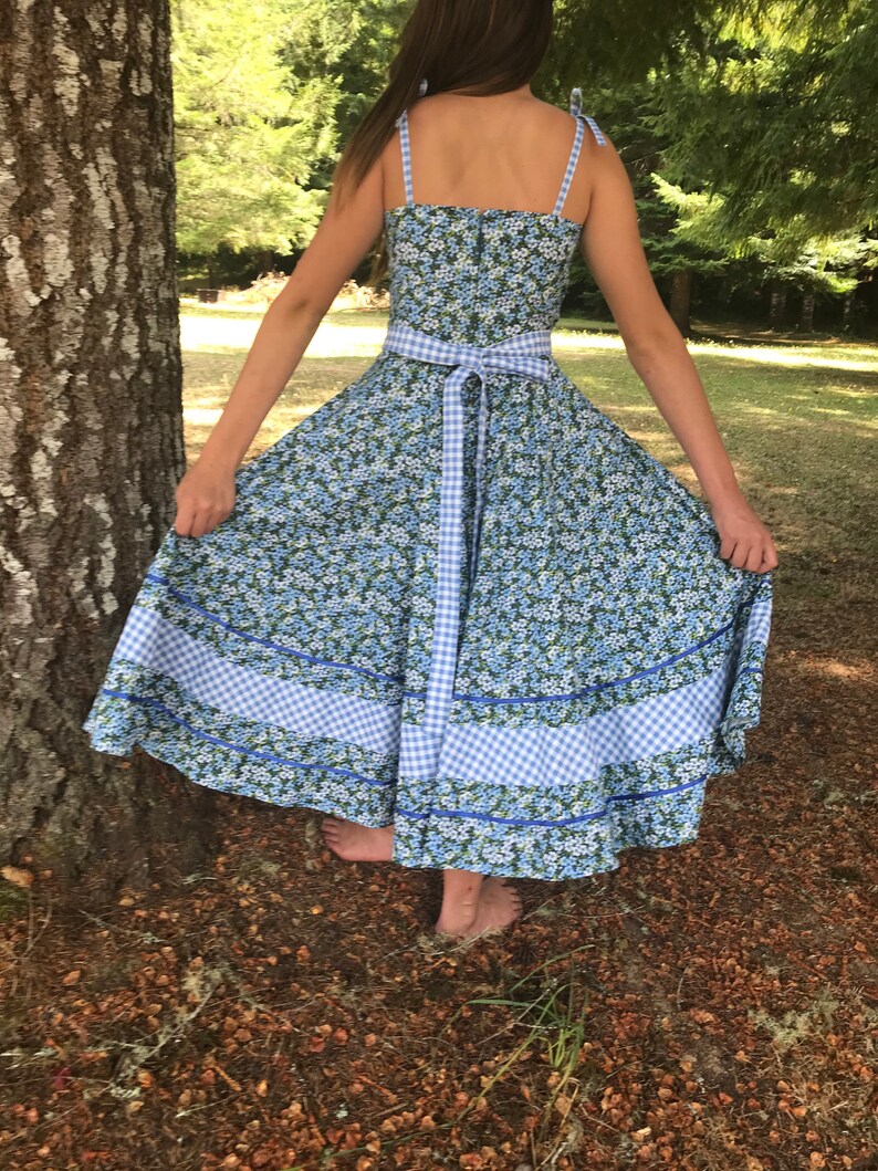 Puede incluir: Un vestido de estampado floral azul y blanco con ribete de vichy y una cinta a juego. El vestido tiene un corpi&ntilde;o ajustado y una falda completa.
