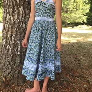 Puede incluir: Un vestido de verano azul y blanco con estampado floral y ribete de vichy. El vestido tiene un corpi&ntilde;o ajustado y una falda completa.