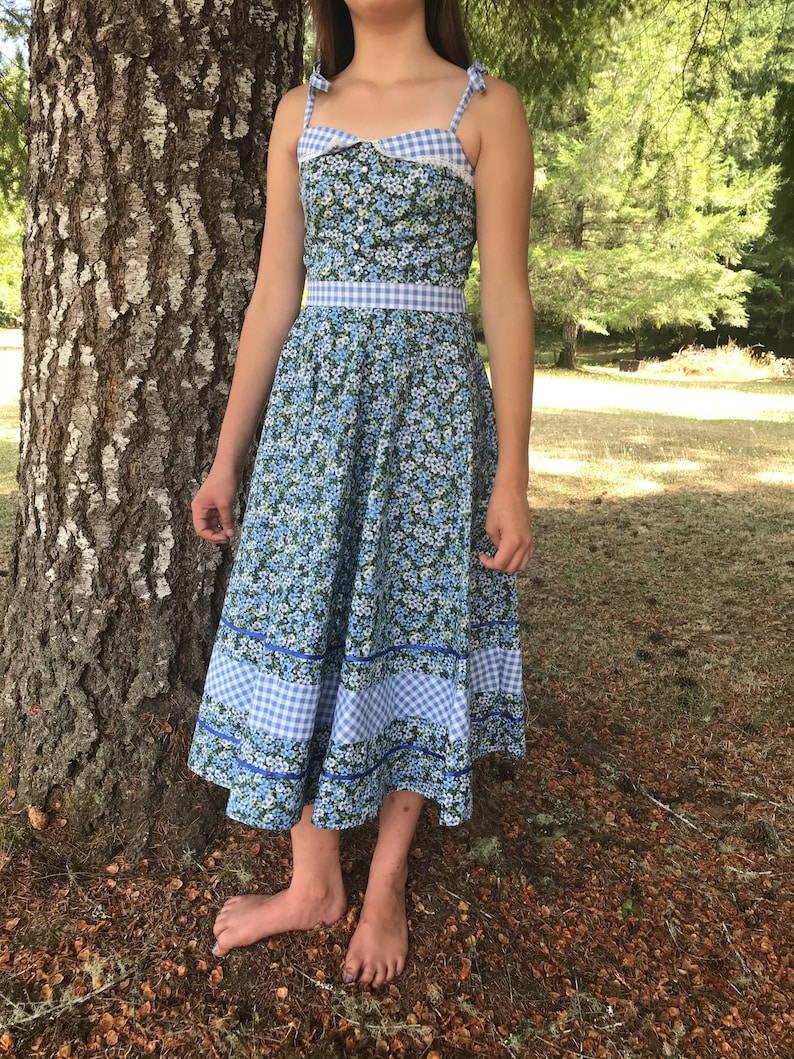 Puede incluir: Un vestido de verano azul y blanco con estampado floral y ribete de vichy. El vestido tiene un corpi&ntilde;o ajustado y una falda completa.