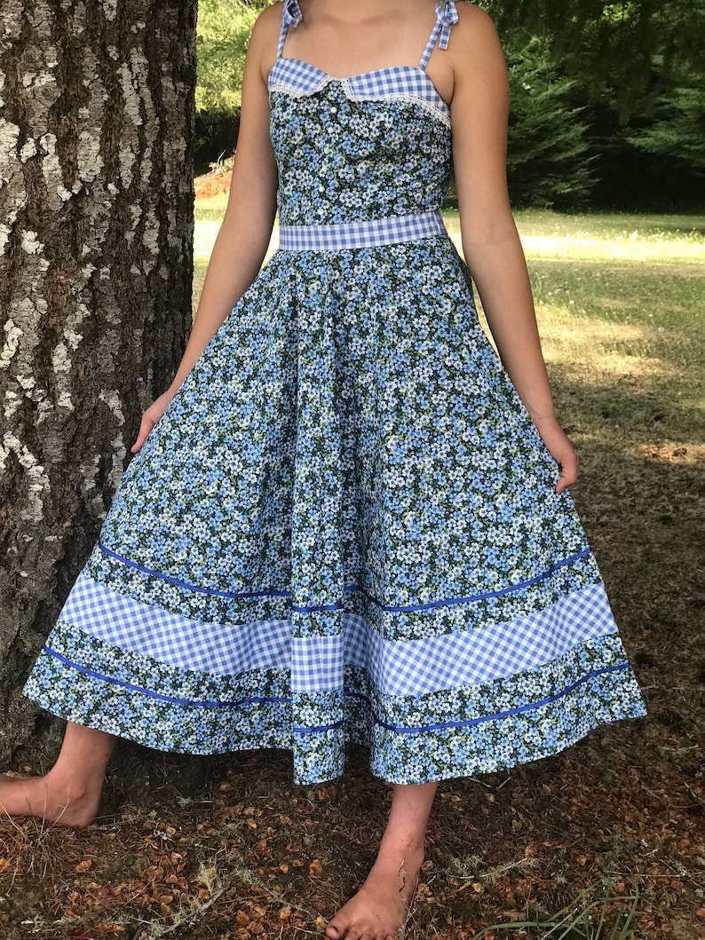 Puede incluir: Un vestido floral azul y blanco con ribete de vichy. El vestido tiene un corpi&ntilde;o ajustado y una falda completa. Las correas son delgadas y se atan en los hombros.
