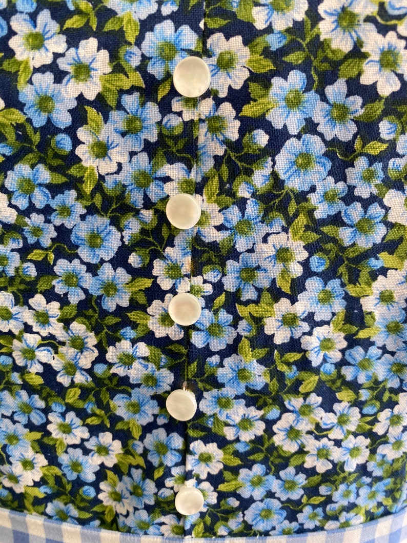 Puede incluir: Primer plano de una tela floral azul y blanca con cinco botones blancos en el centro.