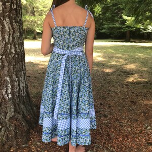 Puede incluir: Un vestido de estampado floral azul y blanco con un lazo de cinta vichy. El vestido tiene un corpi&ntilde;o ajustado y una falda completa.