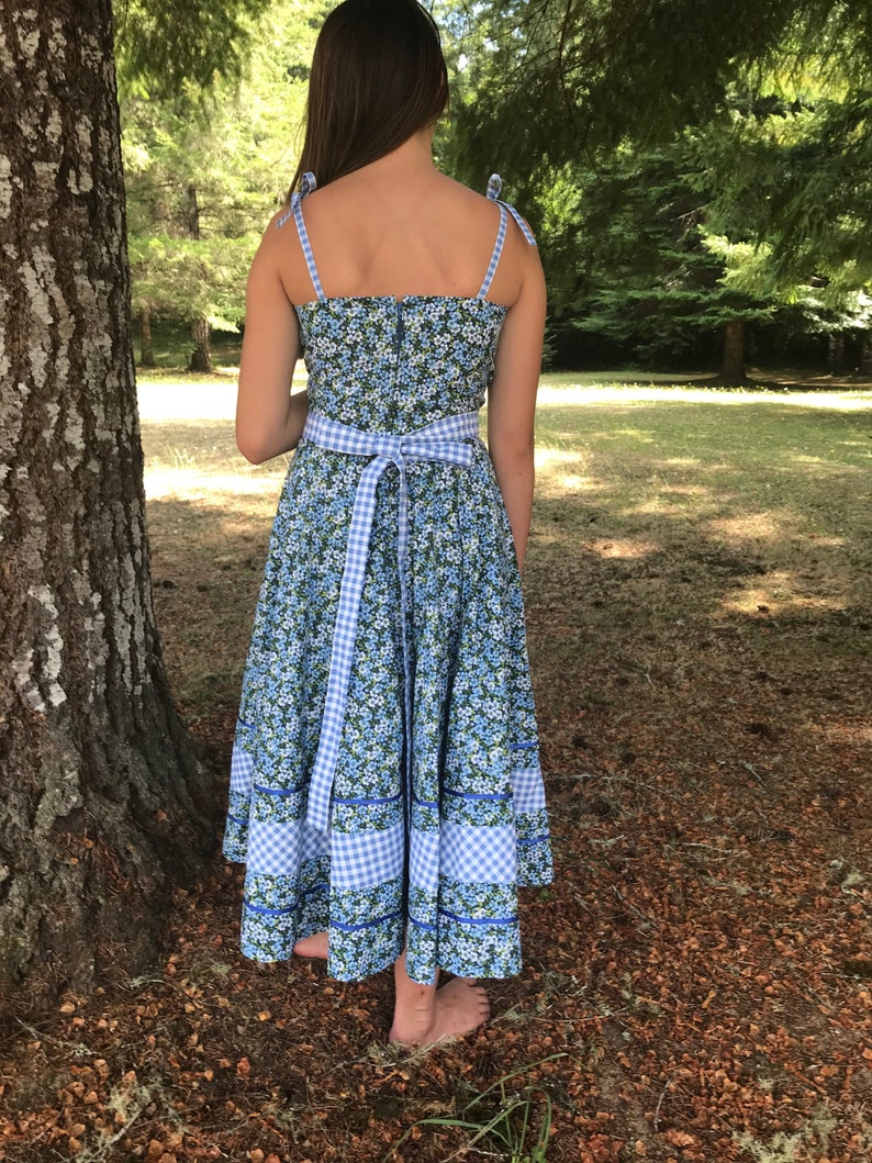 Puede incluir: Un vestido de estampado floral azul y blanco con un lazo de cinta vichy. El vestido tiene un corpi&ntilde;o ajustado y una falda completa.