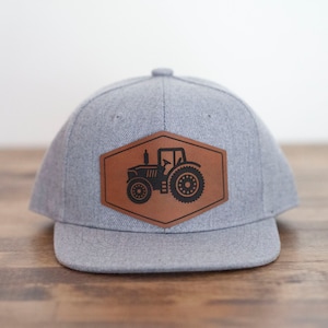 May include: A gray baseball cap with a brown leather patch featuring a black silhouette of a tractor.