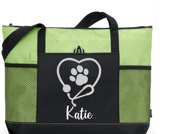 Op de afbeelding: Een zwarte en groene tote bag met een witte pootprint in een hart en een stethoscoop. De naam "Katie" staat onder het hart.