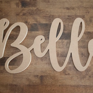 May include: A wooden sign with the name "Bella" written in a cursive font.