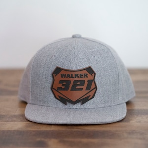May include: Gray baseball cap with a brown leather patch featuring the text "WALKER 321" in black.