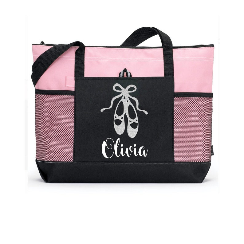 May include: Pink and black tote bag with a mesh pocket and a front pocket featuring a silver glitter ballet shoe design and the name "Olivia" in white.