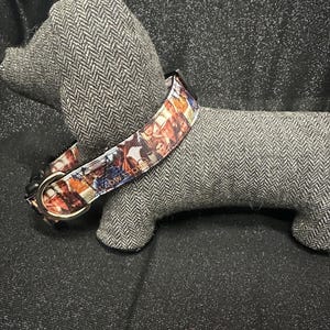 May include: A colorful dog collar with a repeating pattern of images in shades of brown, orange, and blue. The collar is on a gray dachshund-shaped stuffed animal. The collar has a black buckle and a metal ring.