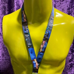 May include: A blue lanyard with the word "TRON" in white and blue text. The lanyard features a repeating pattern of blue and purple images. A gold-colored metal clasp and hook are at the bottom.
