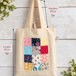 May include: A beige canvas tote bag featuring a central patchwork panel of twelve squares with various floral and geometric patterns. The bag has a length of 32 cm, a width of 27 cm, and handles measuring 20 cm. A small label reads JaneSew Made with love.