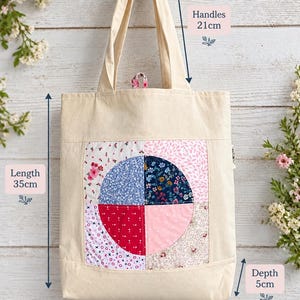 May include: A cream-coloured tote bag featuring a central square patch with a circular design made of four distinct floral and patterned fabric quadrants. The bag has a length of 35cm, a width of 30cm, a depth of 5cm, and handles measuring 21cm.