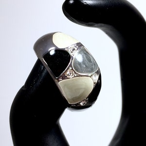 Può includere: Un anello d'argento con smalto nero e bianco e strass trasparenti. L'anello è su un espositore per anelli nero.