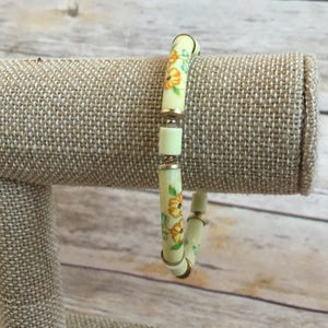 Pulsera con cuentas de porcelana - hallazgos metálicos en tonos dorados - flores pintadas - flores de color naranja amarillo con hojas verdes