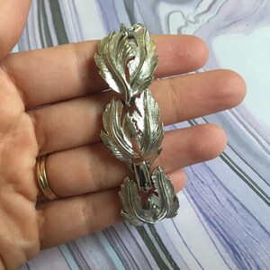 Puede incluir: Pulsera de tono plateado con diseño de hojas. La pulsera está hecha de hojas enlazadas que están conectadas entre sí.