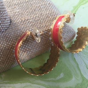 May include: A pair of gold hoop earrings with a red enamel band and a scalloped edge.
