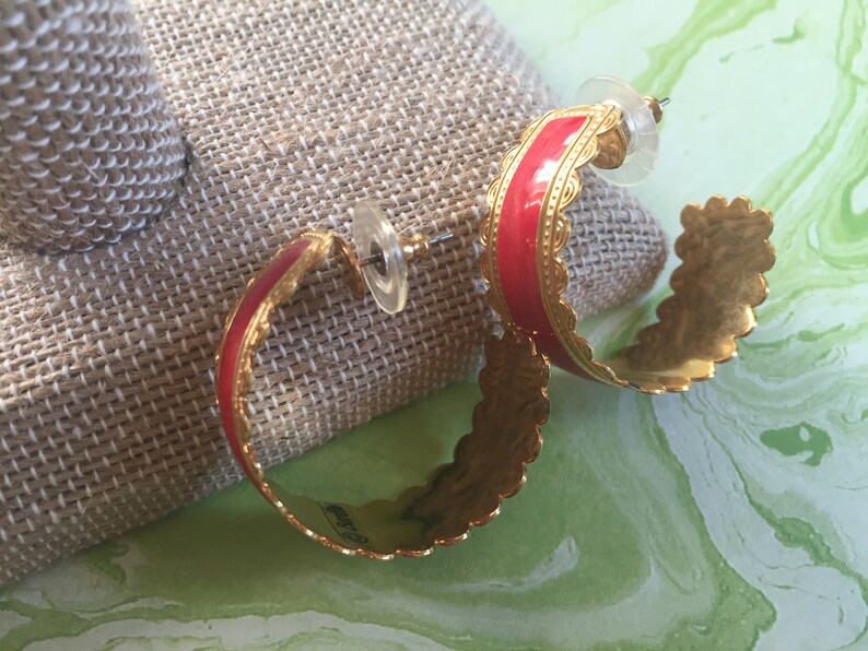 May include: A pair of gold hoop earrings with a red enamel band and a scalloped edge.