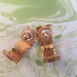 May include: A pair of gold hoop earrings with red accents. The earrings are marked with the word "Barozzi".