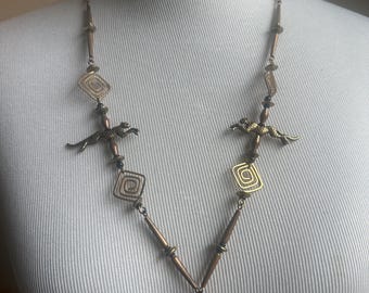 May include: A gold-toned necklace with geometric and animal-shaped pendants. The necklace features three running animal figures and three geometric square-shaped pendants with a swirling pattern.