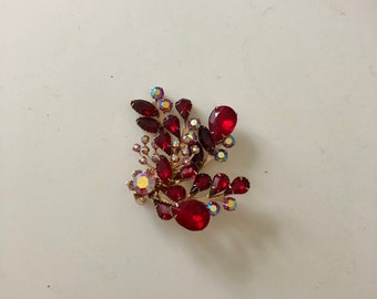 Pode incluir: Um broche de strass vermelho com um design floral. O broche é feito de metal dourado e apresenta uma variedade de strass vermelhos e transparentes.