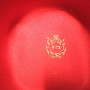 May include: A red felt hat with a gold logo that reads "RITZ 100% Wool HENRY POLLAK INC. NEW YORK"
