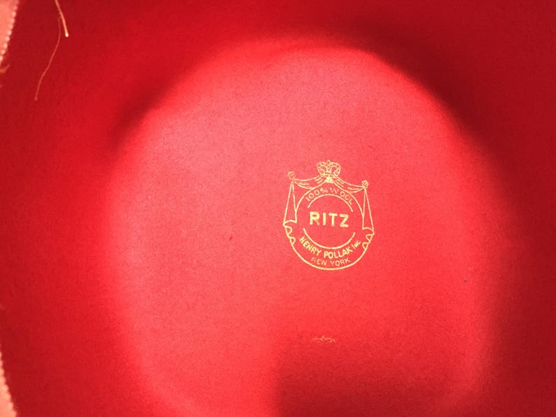 May include: A red felt hat with a gold logo that reads "RITZ 100% Wool HENRY POLLAK INC. NEW YORK"