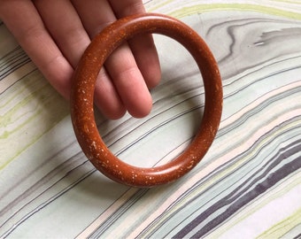 May include: A brown bangle bracelet with a speckled texture.