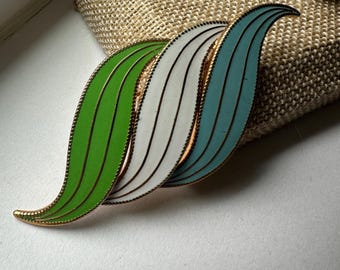 May include: A vintage brooch with three overlapping, wavy, enamel leaves in green, white, and blue colors. The leaves are outlined in gold.