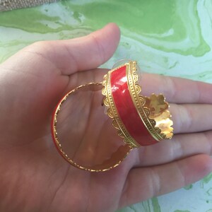 May include: A pair of gold hoop earrings with a red enamel band. The earrings have a decorative scalloped edge.