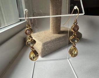 May include: Gold dangle earrings with three teardrop-shaped stones. The stones are a light pink, a light green, and a yellow.