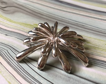 May include: A silver brooch in the shape of a stylized flower with many thin, pointed petals.