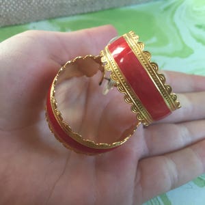 May include: A pair of gold hoop earrings with a red enamel inlay. The earrings have a decorative, scalloped edge.