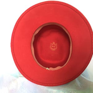May include: A red felt fedora hat with a brown felt band and a gold label that says "RITZ" inside the band.