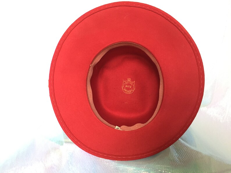 May include: A red felt fedora hat with a brown felt band and a gold label that says "RITZ" inside the band.
