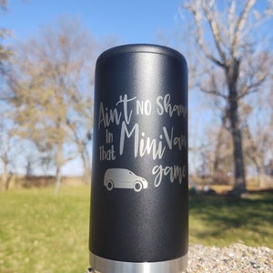 May include: A black stainless steel can cooler with a silver band around the top and bottom. The cooler has an engraved design that says "Ain't no shame in that Mini Van game" with a silhouette of a minivan.