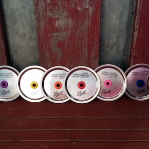 May include: Seven silver metal jar lids with a variety of colored rubber rings. The lids are labeled "crafted-quality seals-for freshness" and "Ball".