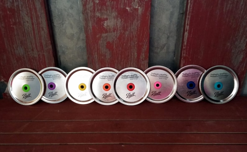 May include: Seven silver metal jar lids with a variety of colored rubber rings. The lids are labeled "crafted-quality seals-for freshness" and "Ball".
