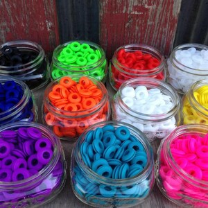 May include: Assortment of colorful plastic grommets in glass jars. The grommets are in various colors, including black, green, red, white, orange, yellow, blue, purple, and pink.