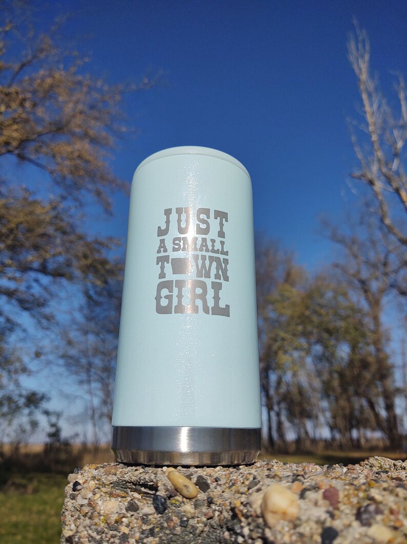May include: A light blue stainless steel tumbler with a silver lid. The tumbler has the text "JUST A SMALL TOWN GIRL" printed on the side.