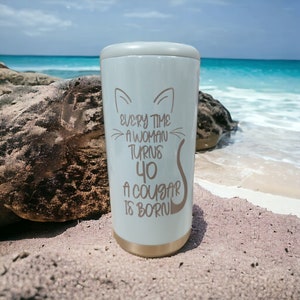 May include: A white stainless steel tumbler with a gold lid and a cat silhouette. The tumbler has the text "Every time a woman turns 40 a cougar is born" printed on it.