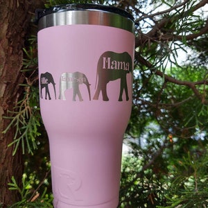 Puede incluir: Un vaso t&eacute;rmico rosa con tapa negra. El vaso presenta tres siluetas de elefantes con los nombres "Allie", "Jameson" y "Mama" grabados en el lateral. Dise&ntilde;ado para mantener las bebidas fr&iacute;as o calientes.