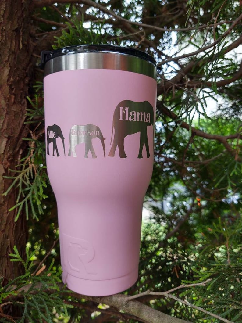 Puede incluir: Un vaso t&eacute;rmico rosa con tapa negra. El vaso presenta tres siluetas de elefantes con los nombres "Allie", "Jameson" y "Mama" grabados en el lateral. Dise&ntilde;ado para mantener las bebidas fr&iacute;as o calientes.