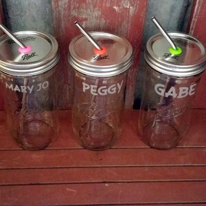 May include: Three clear glass mason jars with metal lids and straws. The jars are labeled "Mary Jo", "Peggy", and "Gabe".