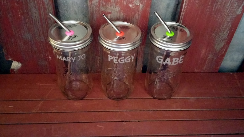 May include: Three clear glass mason jars with metal lids and straws. The jars are labeled "Mary Jo", "Peggy", and "Gabe".