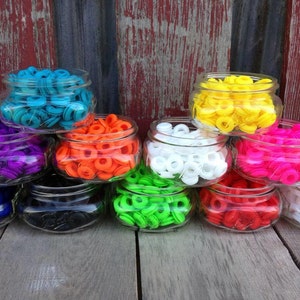 May include: Assortment of colorful plastic rings in glass jars. The rings are in various colors, including blue, purple, orange, white, green, red, and black.