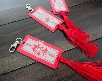 May include: Three rectangular red acrylic keychains featuring silver-toned metal lobster clasps and long red fabric tassels. Each keychain displays a white engraved illustration of an anime-style character with Japanese text within a border.