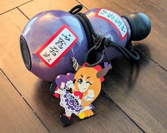 May include: A purple glittery gourd-shaped bottle with a black cap and black cord wrapping. Two rectangular white labels with red borders and black Japanese text are attached. A colorful anime-style character charm hangs from the black cord.
